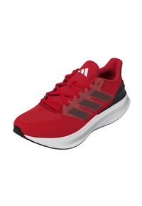 Zapatilla deportiva roja con una parte superior texturizada, diseño de malla y tres rayas negras en el costado. Presenta una entresuela blanca y una suela negra.