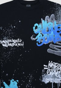 T-shirt nera in cotone con diverse grafiche in blu e bianco, inclusi motivi a spruzzo e testo in grassetto. Collo rotondo.
