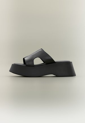 Μαύρο σανδάλι πλατφόρμας με χοντρή σόλα και φαρδιά λουράκι από δέρμα με λεπτομέρεια κοψίματος σε ουδέτερο φόντο.