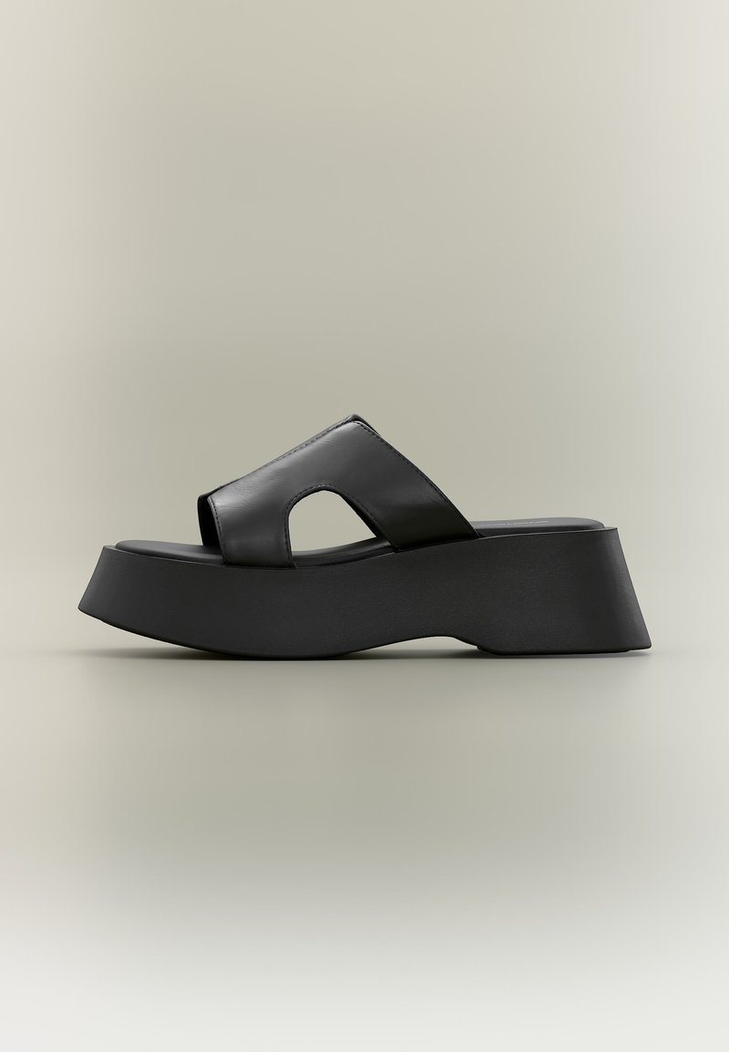 Μαύρο σανδάλι πλατφόρμας με χοντρή σόλα και φαρδιά λουράκι από δέρμα με λεπτομέρεια κοψίματος σε ουδέτερο φόντο.