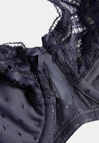 Dunkelblauer Spitzen-BH aus gepunktetem Stoff, mit filigranen Blumenmustern und einem kleinen Satin-Schleifenakzent in der Mitte. Strukturierter Mesh-Überzug.