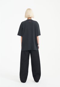 Svart oversized t-shirt i mjuk bomull, med korta ärmar och rund halsringning. Matchad med lösa svarta byxor, sett bakifrån.