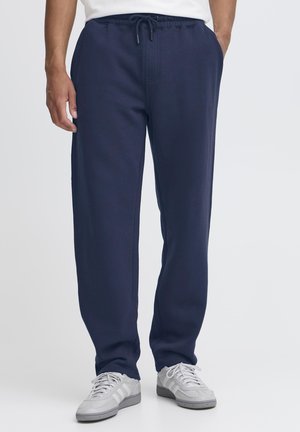 Pantaloni jogger in fleece blu navy con vita elasticizzata, coulisse, tasche laterali e gambe affusolate, abbinati a scarpe da ginnastica grigie.