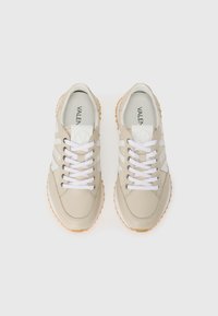 Baskets beiges en cuir lisse, avec des accents blancs, bout rond et semelle en caoutchouc avec une texture antidérapante. Les lacets sont blancs.