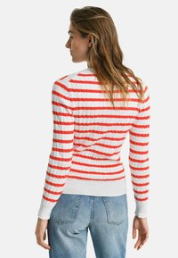 Rot-weiß gestreifter Rippenstrickpullover mit langen Ärmeln und tailliertem Schnitt. Weiße Bündchen und Saum, kombiniert mit blauen Jeans.