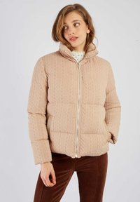 Kurtka puchowa z miękkiego różowego dzianiny, z wysokim kołnierzem, zamkiem błyskawicznym i teksturowanym wzorem. Dobana do brązowych spodni sztruksowych.