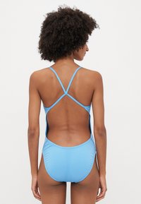 Bañador azul claro con una espalda baja y tirantes entrecruzados. Textura suave, diseño minimalista y escote alto en las piernas.