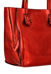 Punainen nahkainen olkalaukku, jossa on kaksi solmittua kahvaa ja sileä pintatekstuuri, valkoisen taustan edessä.