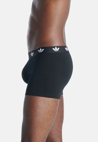 Svarta bomullsboxershorts med svart midjeband som har upprepade vita Adidas trefoil-loggor. Tätt sittande och med en slät yta.