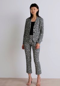Grau gemusterte Blazer und passende Hose aus leichtem Material. Das Outfit zeichnet sich durch ein geometrisches Design mit subtilen Farbakzenten aus.