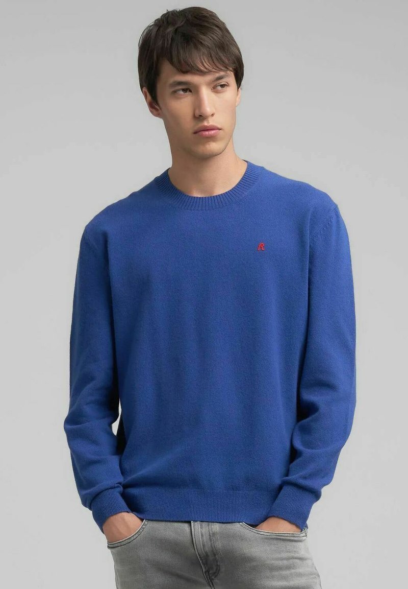 Maglione blu lavorato a maglia con scollo rotondo, polsini e orlo a coste. Presenta un piccolo logo rosso sul petto sinistro. Texture morbida e design aderente.