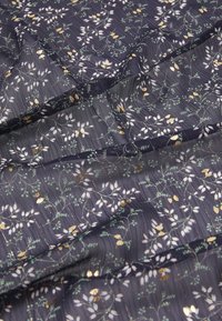 Tissu bleu marine avec un motif floral comprenant des feuilles blanches et des accents dorés. La texture semble douce avec un plissage subtil.