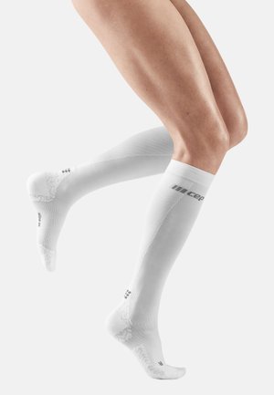 White compression socks with a textured pattern, fitted design, and reinforced toe area, featuring a logo on the calf and arch.
