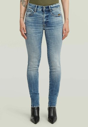 Jeans aderenti azzurri chiaro con effetto slavato, vita media, passanti per cintura, tasche anteriori, chiusura con bottone, indossati con stivali neri a punta.