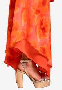 Jupe en chiffon floral orange avec un ourlet superposé, associée à des sandales à talons bloc métalliques dorées avec un design à lanières et une boucle autour de la cheville.