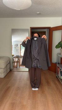 Mørkeblå stribet blazer holdes op, med en glat indvendig foring. Personen bærer brune bukser og hvide sokker, indendørs.
