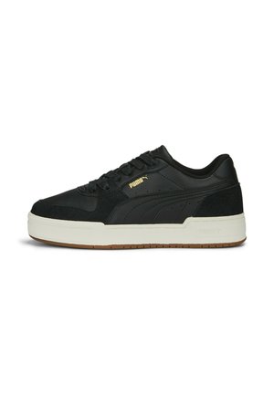 Zapatilla negra con materiales de cuero y ante, diseño de cordones, suela intermedia gruesa blanca y suela de goma marrón. Presenta un acento de logo dorado.