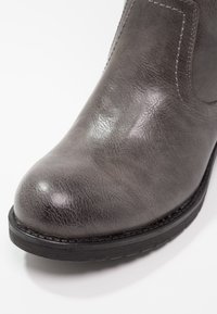 Bottine en cuir gris avec un bout arrondi, une finition texturée, des panneaux latéraux élastiques et une semelle en caoutchouc noire. Coutures visibles en accent.