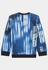 Felpa blu con un design a gradiente che presenta testo bianco, inclusi "GUESS" e "FONDATA NEL 1981". Collo e polsini a costine.