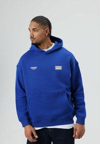 Blauwe hoodie gemaakt van een katoenmengsel, met een voorzak, een capuchon met trekkoord en bedrukte logo's op de borst. Geribbelde manchetten en zoom.