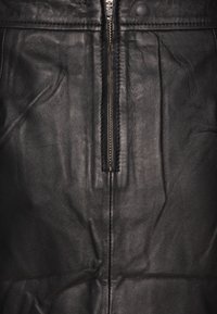 Veste en cuir noir avec une fermeture éclair centrale, surface texturée, coutures visibles et coupe ajustée. Présente une finition lisse et noire.