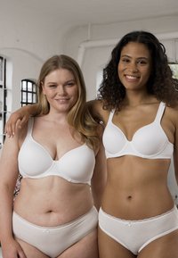 Witte bh's met gladde cups en verstelbare bandjes, gecombineerd met bijpassende witte slips met kantafwerking, getoond door twee modellen.