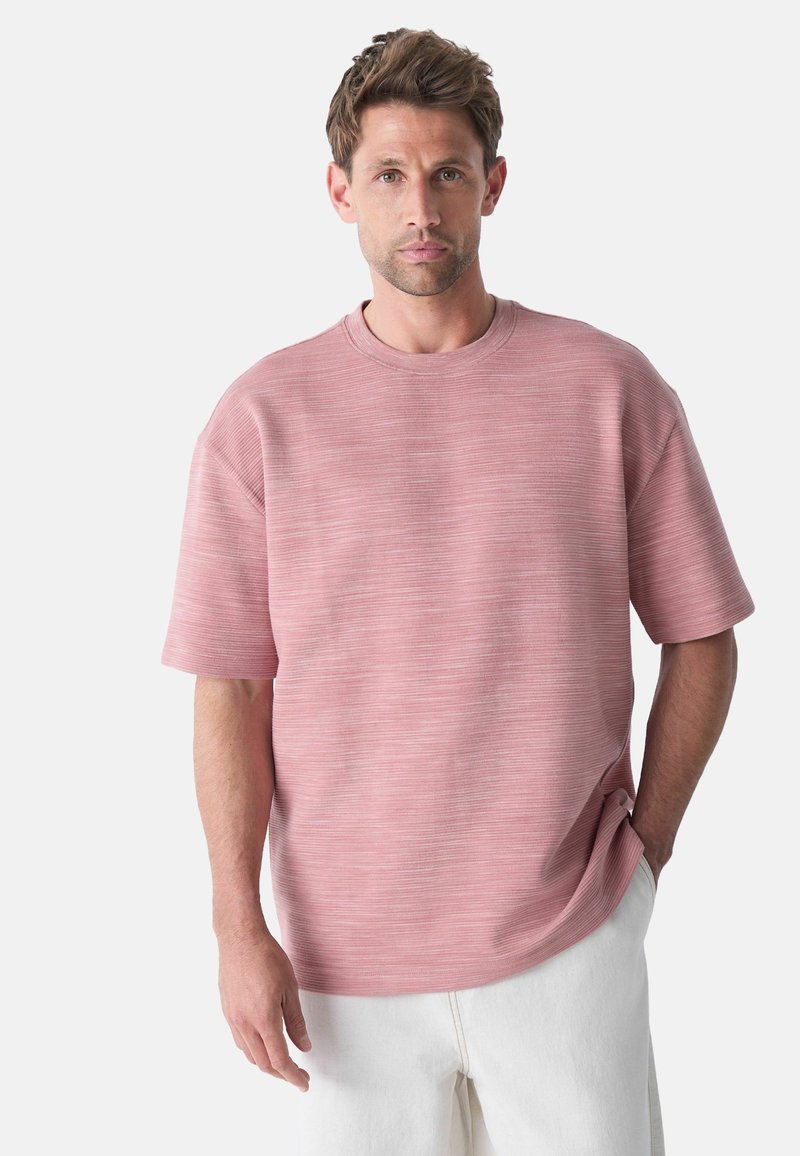 Camiseta corta de manga corta color rosa claro con un corte relajado, tela texturizada, escote redondo y rayas horizontales, combinada con pantalones blancos.