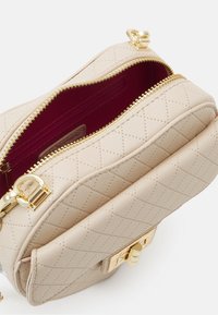 Beżowa pikowana skórzana torebka z złotymi elementami, otwarty suwak na górze odsłania głębokie czerwone wnętrze oraz wewnętrzną kieszeń na zamek.