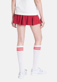 Červená plisovaná suknička, bílé ponožky po kolena s červenými pruhy a bílé tenisky. Jednoduchý design s neformální sportovní estetikou.