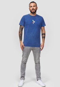 Modré bavlněné tričko s kulatým výstřihem a vyšitým designem na hrudi. Kombinováno se šedými slim fit džíny a bílými teniskami.