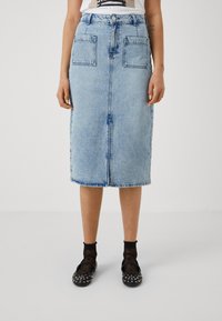 Fustă din denim albastru deschis, cu un croi până la genunchi, buzunare frontale și un talie clasică cu închidere cu button. Marginea uniformă și decolorare subtilă.