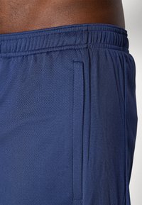Navy blue athletic shorts made of mesh fabric with an elastic waistband and side pockets, showcasing a textured surface and clean seams.