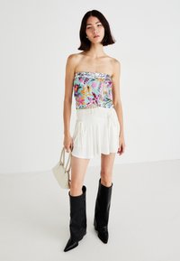 Strapless, gekleurde bloes met pailletten en franjes. Gecombineerd met een witte geplooide mini-jurk en zwarte kniehoge laarzen.