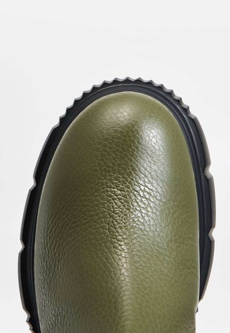 Zielony skórzany but z okrągłym czubkiem i teksturowaną powierzchnią, wyposażony w grubą czarną podeszwę z rowkami zapewniającymi przyczepność.