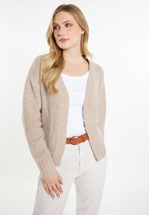 Beige cardigan gemaakt van zacht, gestructureerd materiaal, met ribgebreide manchetten en een open voorkant. Draag het over een witte top met een bruine riem.