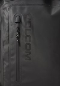Sort vandtæt taske med en glat overflade, lynlåslomme og præget "VOLCOM" logo. Designet til holdbarhed og funktionalitet.