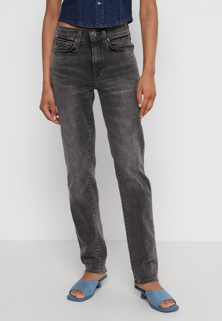 Hoch geschnittene schwarze Denim-Jeans mit geradem Bein, ausgewaschenem Look, vorderen Taschen und kontrastierenden Nähten, kombiniert mit blauen Rutsch-Sandalen.