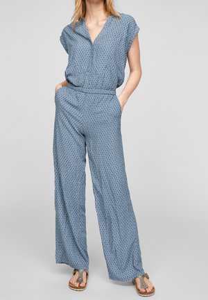 Blå mønstret jumpsuit med V-hals, korte ærmer, afslappet pasform, elastisk talje og bukser med vidde. Bruges med flade sandaler.