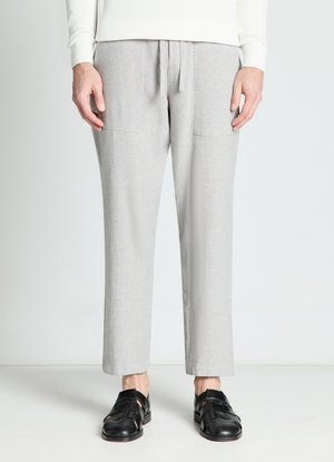 Uomo che indossa pantaloni grigio chiaro a gamba dritta con tasche applicate sul davanti e sandali neri in pelle, in piedi davanti a uno sfondo bianco uniforme.