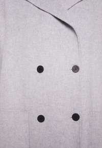 Manteau en laine gris clair à double boutonnage avec quatre boutons noirs et un large col.