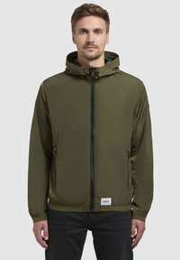 Leichtgewichtige olivgrüne Jacke mit Kapuze, durchgehendem Reißverschluss vorne, seitlichen Taschen, elastischen Bündchen und einem Logopatch am Saum.
