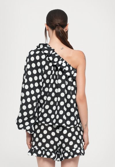 Schwarz-weißer Polka-Dot-Top mit einem Schulterträger, gerafftem Ausschnitt und fließendem Stoff. Kombiniert mit passenden Shorts mit gefransten Säumen.