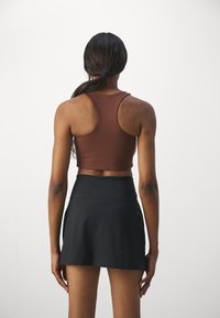 Brun crop top med racerback-design, parret med en sort skort. Glat stof med tætsiddende silhuet, der fremhæver ryggen og taljen.