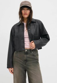 Veste en cuir noir coupée avec col, fermeture à boutons et deux poches avant ; associée à un haut rose clair et un jean vert délavé.