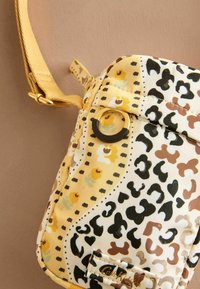 Borsa a tracolla con stampa leopardata, caratterizzata da motivi gialli e bianchi, un accento con anello dorato e una tracolla testurizzata con chiusura metallica. Design compatto.