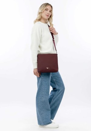 Sac bandoulière bordeaux en matériau lisse, avec un discret logo en accent, encadré par une forme rectangulaire et une sangle réglable.