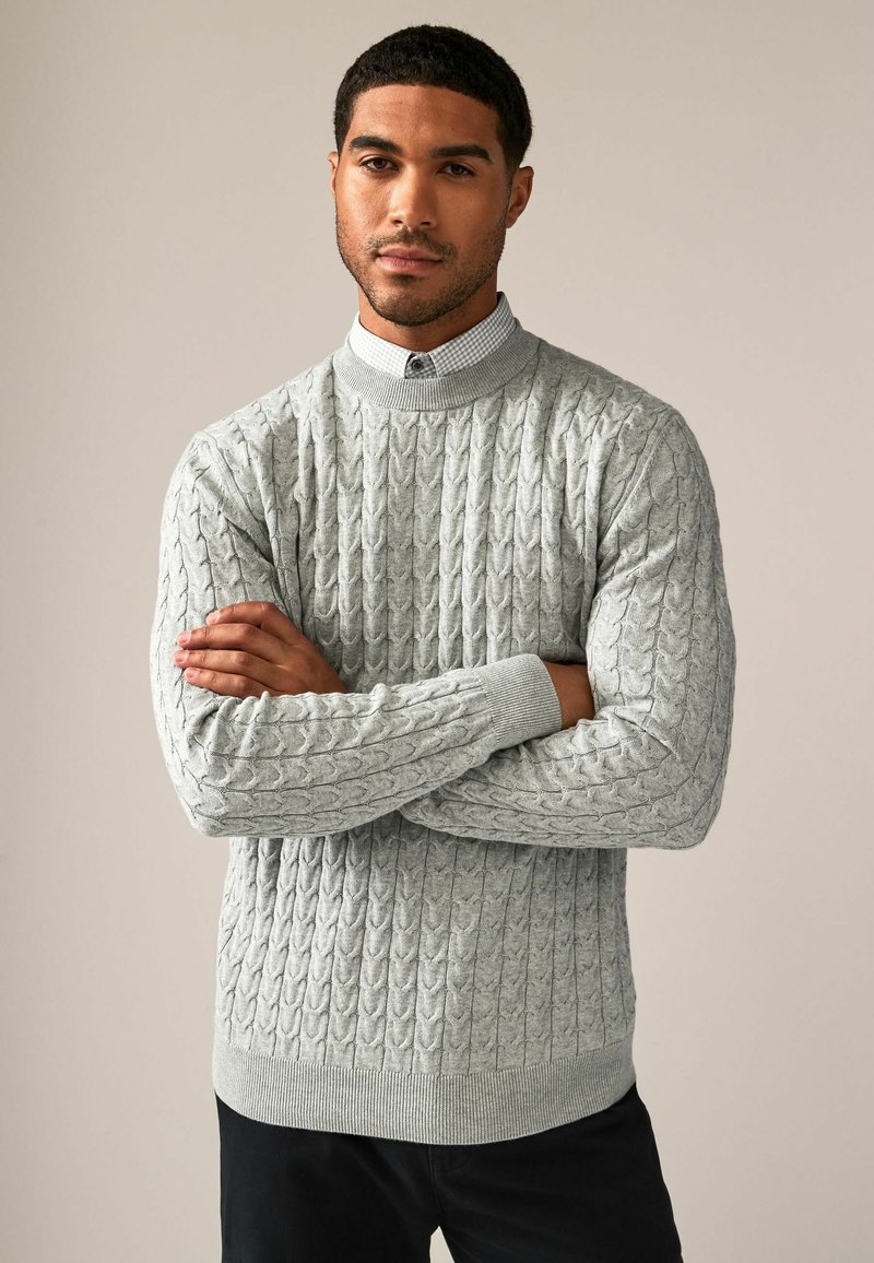 Pull en maille torsadée gris clair avec un col haut, des poignets côtelés et une ceinture côtelée. Stylé avec une chemise à col contrastante en dessous.