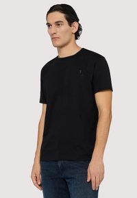 Svart bomulls t-shirt med rund hals och korta ärmar. Har en diskret logotyp på bröstet. Matchas med mörkblå denimjeans.