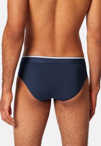 Marineblaue Herrenunterwäsche mit einem elastischen Bund in Weiß, aus einem glatten, dehnbaren Stoff gefertigt, mit enger Passform und minimaler Bedeckung.