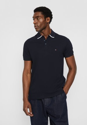 Polo shirt blu navy con colletto bianco, patta con tre bottoni e piccolo logo sul petto. Tessuto morbido e design aderente.